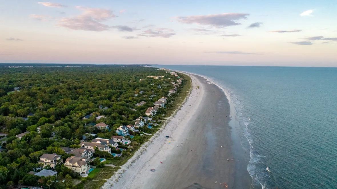 An aerial view of Hilton Head’s coastline where pine trees and luxurious homes stretch to meet sandy beaches and blue waters.