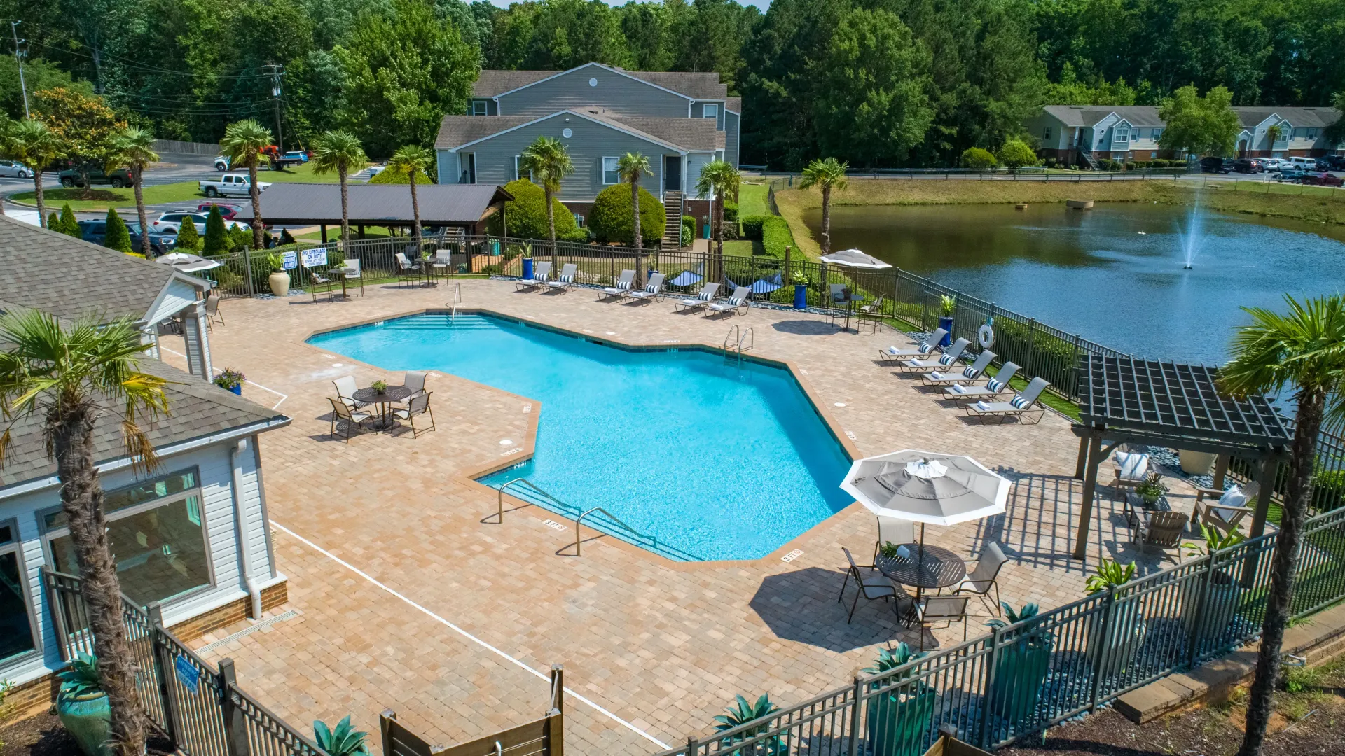 From above, the shimmering pool, extensive deck, lush greenery, and tranquil lake with a fountain create a breathtaking vista.