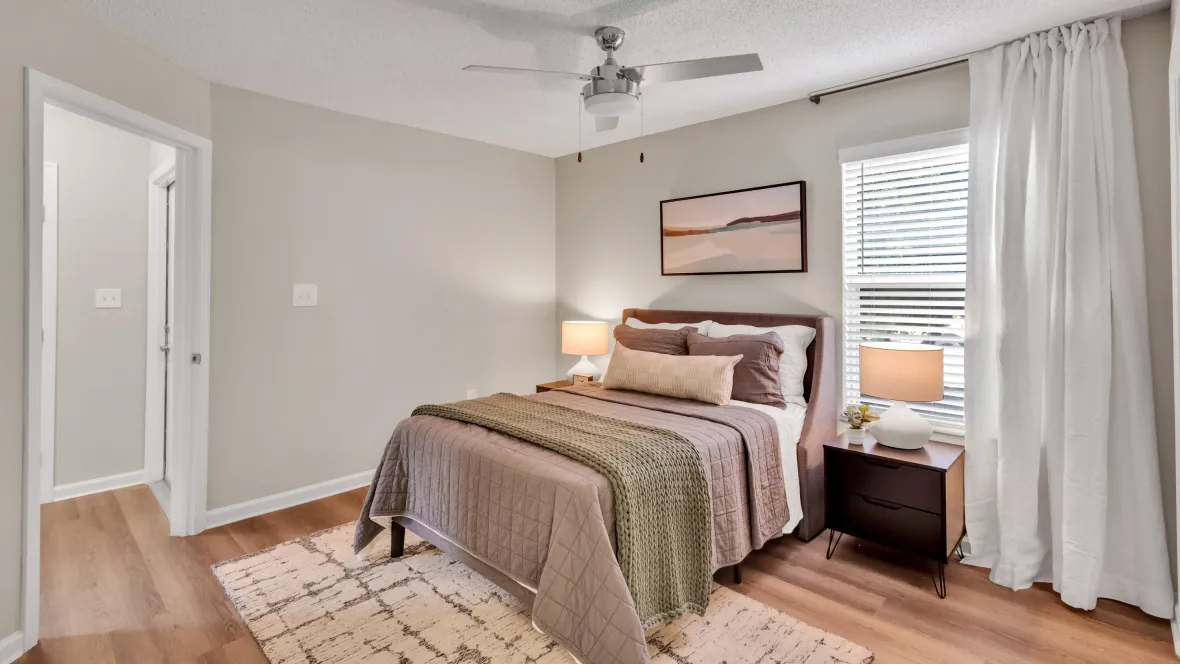 An upgraded bedroom with warm wood-style flooring, a contemporary ceiling fan, and a generously sized closet with built-in shelving.