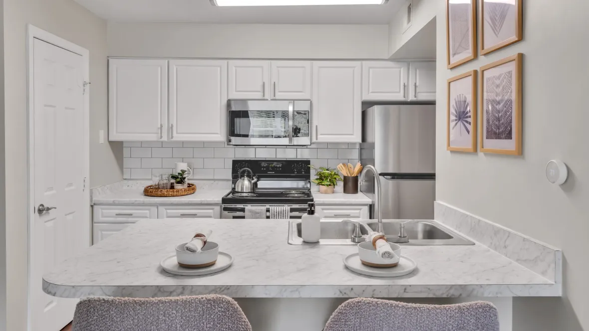 A stunning, brightly lit kitchen featuring beautiful white cabinetry, Carrara countertops, and a subway tile backsplash.